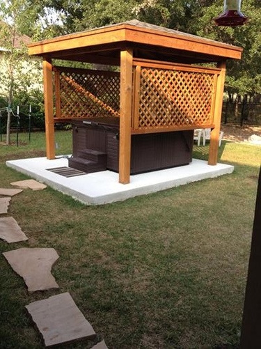 a hot tub positioned on a cement pad in a backyard with a protective wooden gazebo